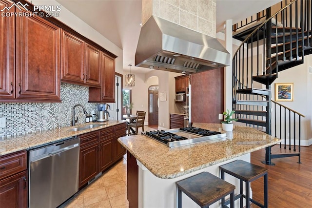 kitchen with a breakfast bar area, a sink, backsplash, exhaust hood, and stainless steel appliances