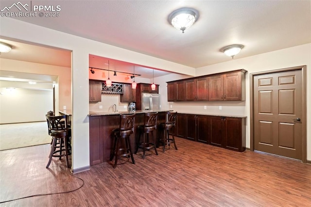 kitchen with a peninsula, a kitchen bar, dark wood-type flooring, stainless steel fridge with ice dispenser, and a sink