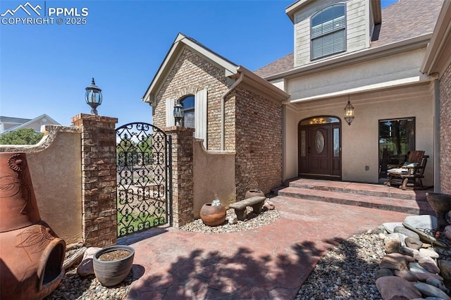 entrance to property with covered porch, brick siding, a shingled roof, and a gate