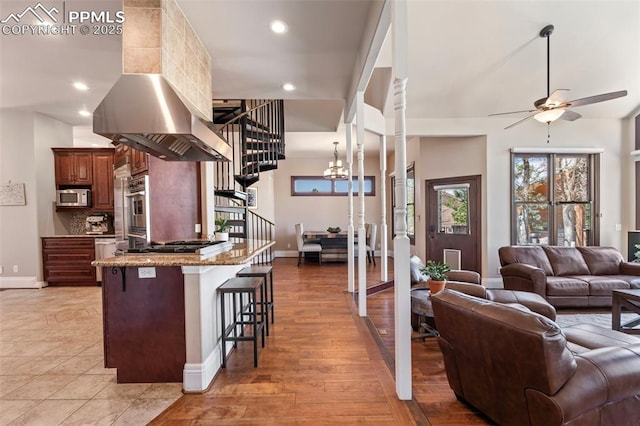 kitchen with a breakfast bar area, gas stovetop, stainless steel microwave, ceiling fan with notable chandelier, and open floor plan