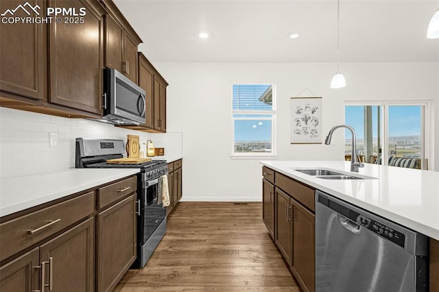 kitchen featuring dark wood-style flooring, appliances with stainless steel finishes, a sink, light countertops, and decorative backsplash