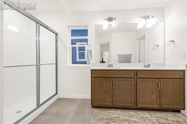 bathroom featuring double vanity, baseboards, a sink, and a stall shower