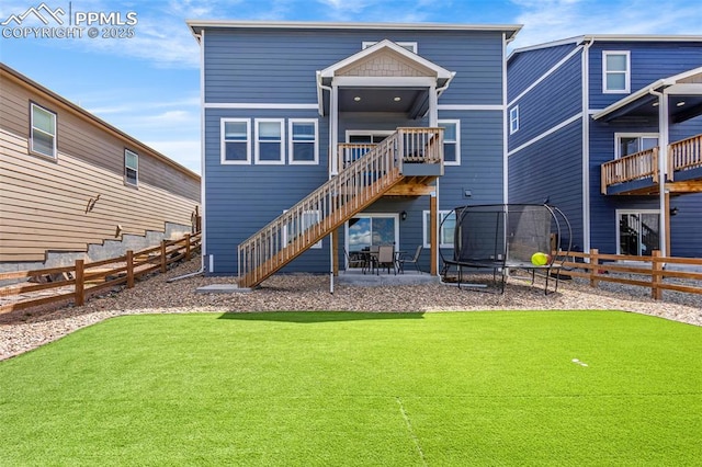 rear view of house featuring a lawn, a fenced backyard, a trampoline, and stairway