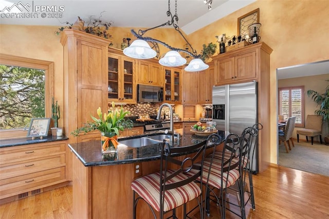 kitchen featuring appliances with stainless steel finishes, a kitchen island with sink, light wood-style flooring, tasteful backsplash, and visible vents