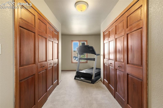 workout room with light colored carpet, a textured wall, and baseboards