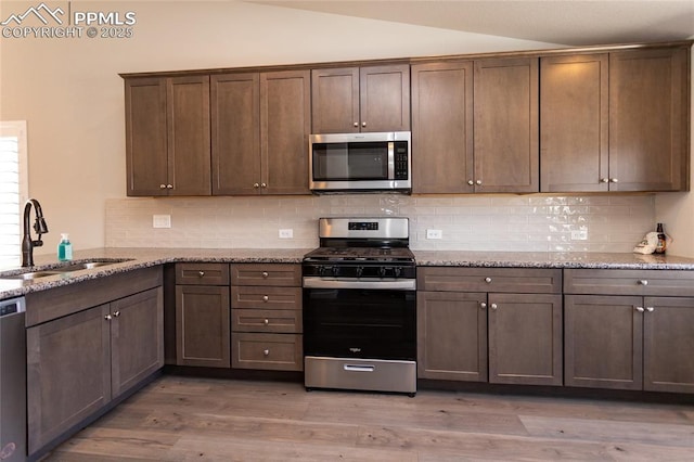 kitchen featuring appliances with stainless steel finishes, tasteful backsplash, a sink, light wood finished floors, and lofted ceiling