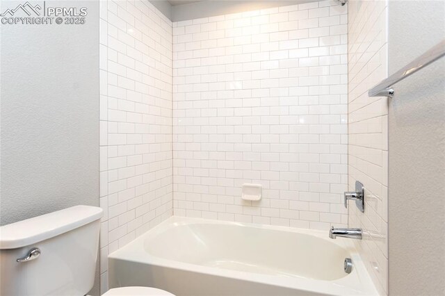 bathroom with toilet, a textured wall, and tub / shower combination