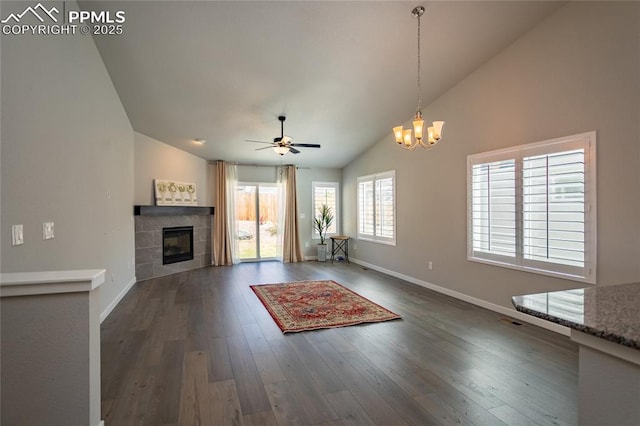 unfurnished living room with a tiled fireplace, baseboards, high vaulted ceiling, ceiling fan with notable chandelier, and dark wood-type flooring
