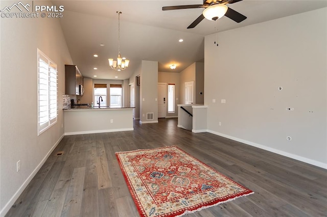 unfurnished living room featuring a sink, ceiling fan with notable chandelier, lofted ceiling, dark wood-type flooring, and visible vents