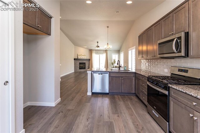 kitchen with light stone countertops, a tiled fireplace, a sink, vaulted ceiling, and stainless steel appliances
