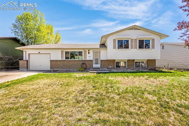 tri-level home with driveway, a front yard, a garage, brick siding, and fence