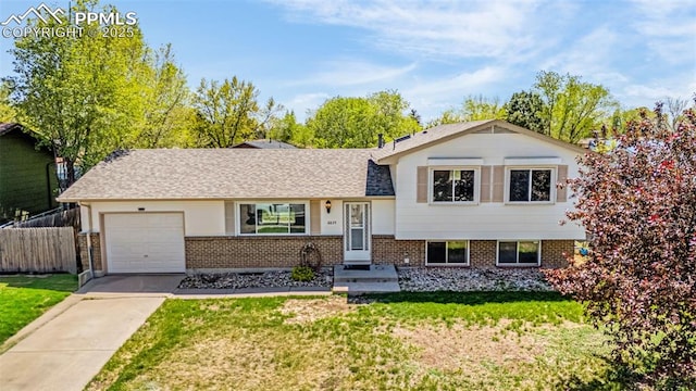 tri-level home featuring brick siding, fence, a front lawn, concrete driveway, and an attached garage