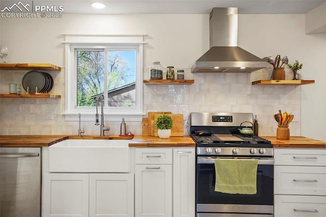 kitchen with open shelves, a sink, wall chimney exhaust hood, stainless steel appliances, and butcher block counters