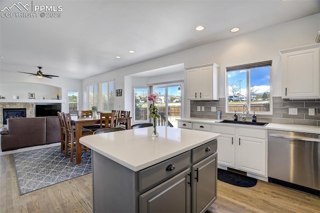 kitchen featuring a ceiling fan, stainless steel dishwasher, a fireplace, a sink, and light wood-style flooring