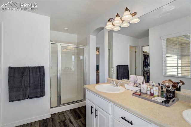bathroom featuring double vanity, a shower stall, a sink, and wood finished floors