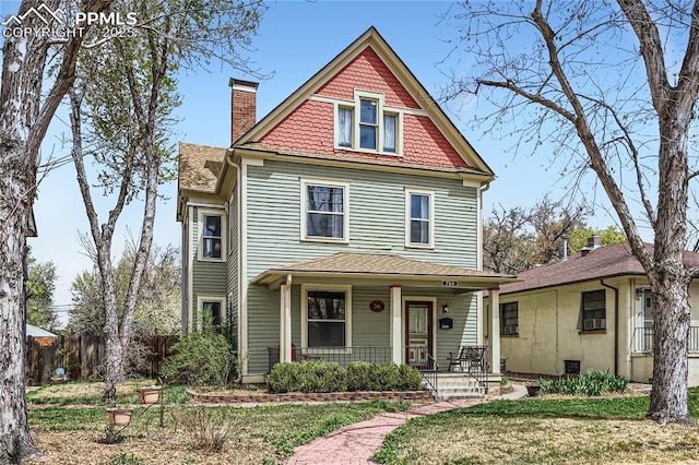 victorian-style house with a chimney, roof with shingles, covered porch, and fence