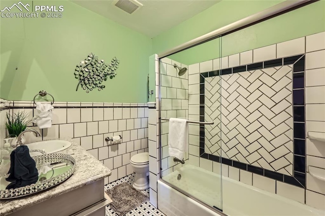 full bath with toilet, tile walls, visible vents, bath / shower combo with glass door, and vanity