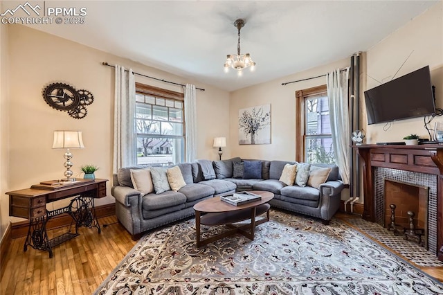 living room featuring an inviting chandelier, a wealth of natural light, a tiled fireplace, and hardwood / wood-style flooring