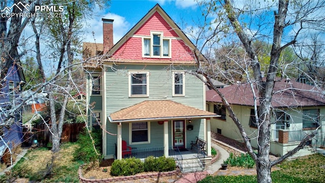 victorian-style house featuring covered porch, a shingled roof, and a chimney