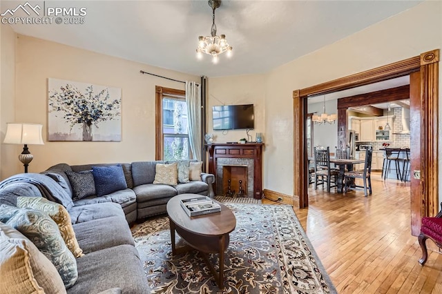 living area featuring baseboards, hardwood / wood-style floors, an inviting chandelier, and a fireplace with flush hearth