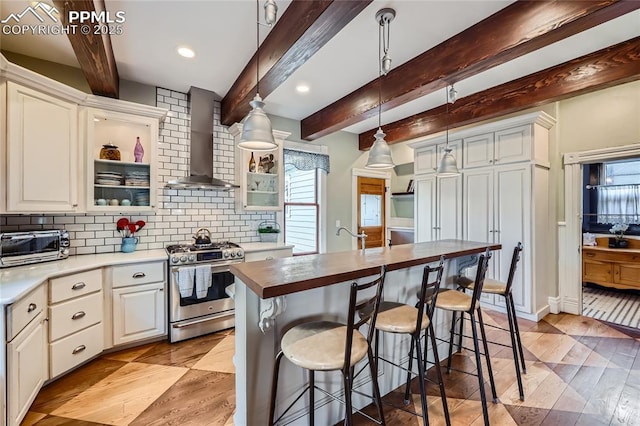 kitchen with stainless steel range with gas stovetop, a healthy amount of sunlight, decorative backsplash, and wall chimney exhaust hood
