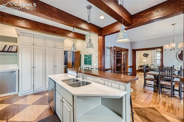 kitchen featuring pendant lighting, dishwasher, a sink, a center island with sink, and beam ceiling