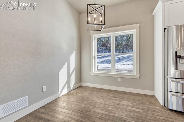 unfurnished dining area with visible vents, wood finished floors, baseboards, and a notable chandelier