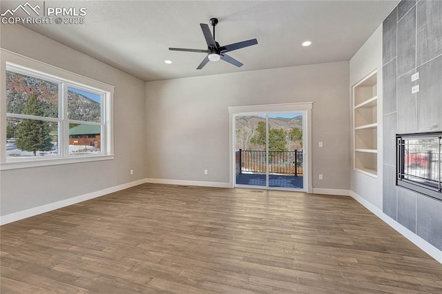 unfurnished living room featuring baseboards, ceiling fan, built in features, and wood finished floors