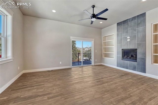 unfurnished living room with wood finished floors, baseboards, ceiling fan, built in shelves, and recessed lighting