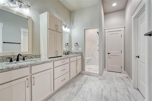 bathroom with a marble finish shower, double vanity, a sink, and a textured wall
