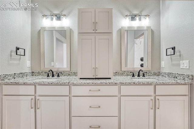 bathroom with double vanity, a sink, and a textured wall