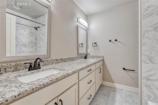 full bathroom featuring a sink, double vanity, a textured wall, and baseboards