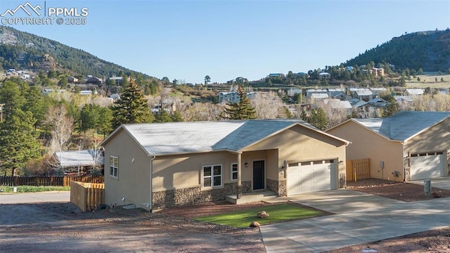 single story home featuring stone siding, a mountain view, a garage, stucco siding, and fence