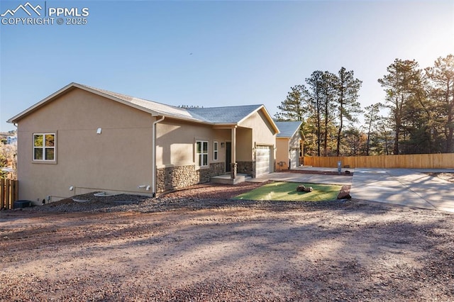 view of home's exterior with stone siding, a garage, stucco siding, fence, and driveway