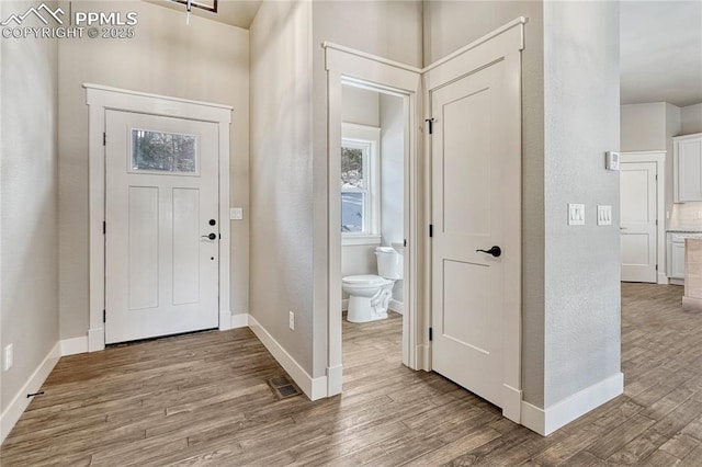 foyer featuring a textured wall, baseboards, visible vents, and wood finished floors