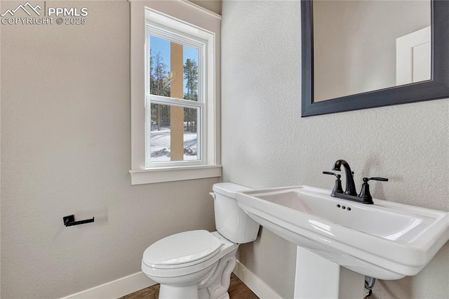 bathroom with toilet, wood finished floors, a sink, baseboards, and a textured wall