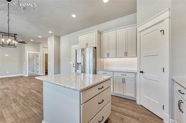 kitchen featuring tasteful backsplash, wood finished floors, stainless steel refrigerator with ice dispenser, a center island, and a notable chandelier