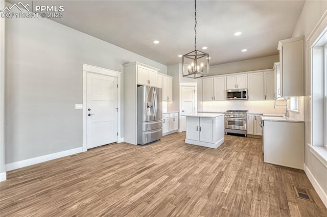 kitchen with light wood finished floors, a kitchen island, stainless steel appliances, visible vents, and a chandelier