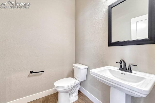 half bath featuring toilet, wood finished floors, baseboards, and a sink