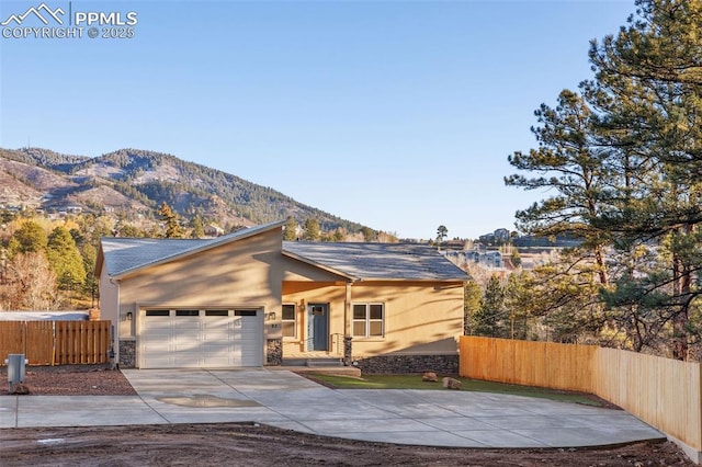 view of front facade featuring fence, an attached garage, stone siding, a mountain view, and driveway
