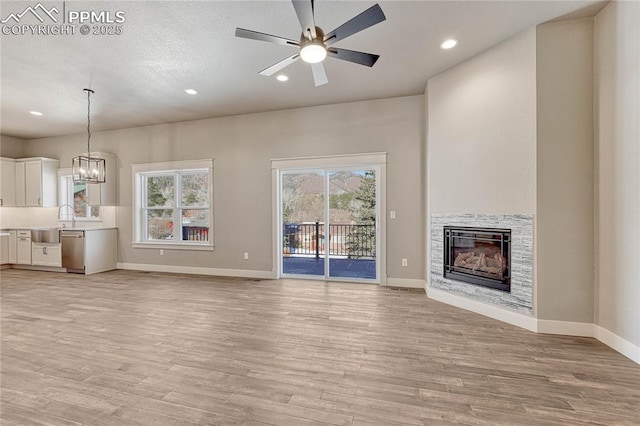 unfurnished living room featuring baseboards, a stone fireplace, light wood-style flooring, and recessed lighting