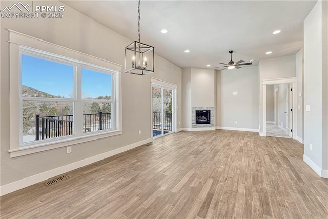 unfurnished living room featuring baseboards, light wood-style floors, visible vents, and ceiling fan with notable chandelier
