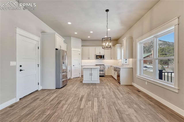 kitchen with a sink, a kitchen island, light wood-style floors, light countertops, and appliances with stainless steel finishes