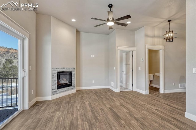 unfurnished living room with a fireplace, ceiling fan with notable chandelier, plenty of natural light, and wood finished floors