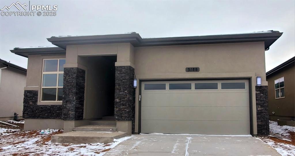 prairie-style house featuring stucco siding, concrete driveway, and stone siding