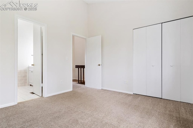 unfurnished bedroom with a closet, a towering ceiling, ensuite bath, carpet flooring, and baseboards