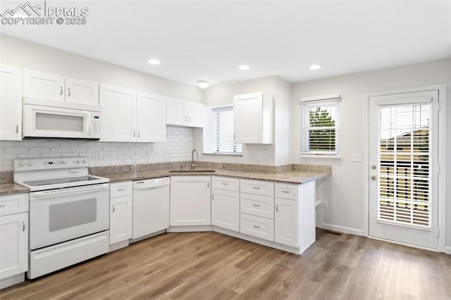 kitchen featuring light wood finished floors, a sink, white cabinets, white appliances, and decorative backsplash