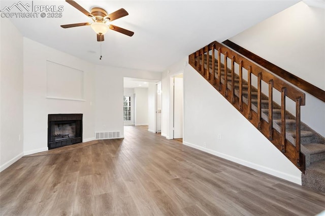 unfurnished living room featuring wood finished floors, a ceiling fan, a fireplace, visible vents, and stairs
