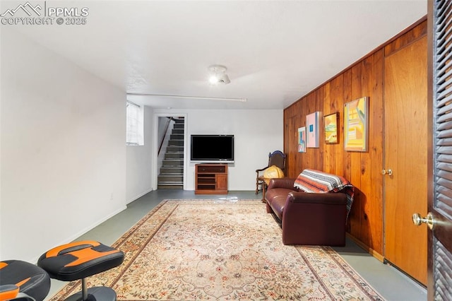 living room featuring baseboards, stairs, wooden walls, and concrete floors
