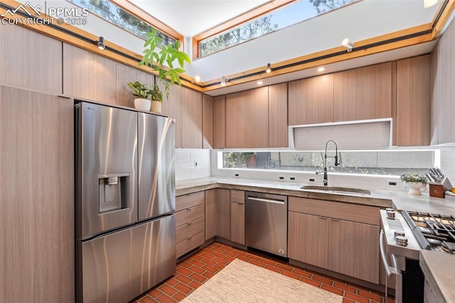 kitchen with decorative backsplash, light countertops, brick floor, a sink, and appliances with stainless steel finishes
